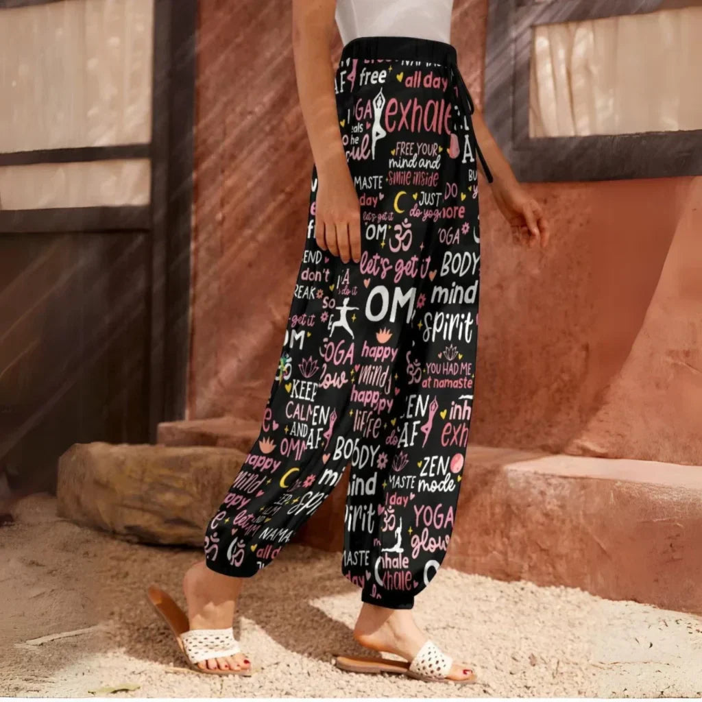 Loose-fitting harem pants with yoga-themed text and words printed all over in pink and white on black fabric, side view - YOGA QUOTES HAREM PANTS WOMEN - SPIRITUAL COMFORT