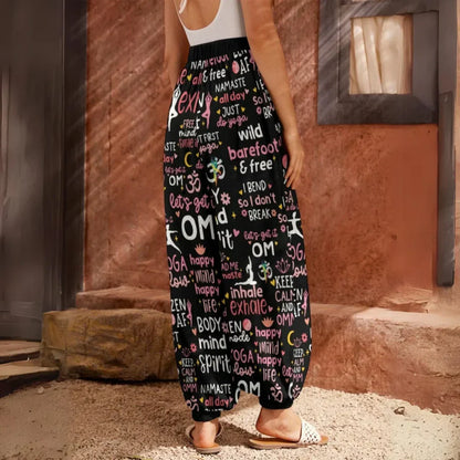 Loose-fitting harem pants with yoga-themed text and words printed all over in pink and white on black fabric, back view - YOGA QUOTES HAREM PANTS WOMEN - SPIRITUAL COMFORT