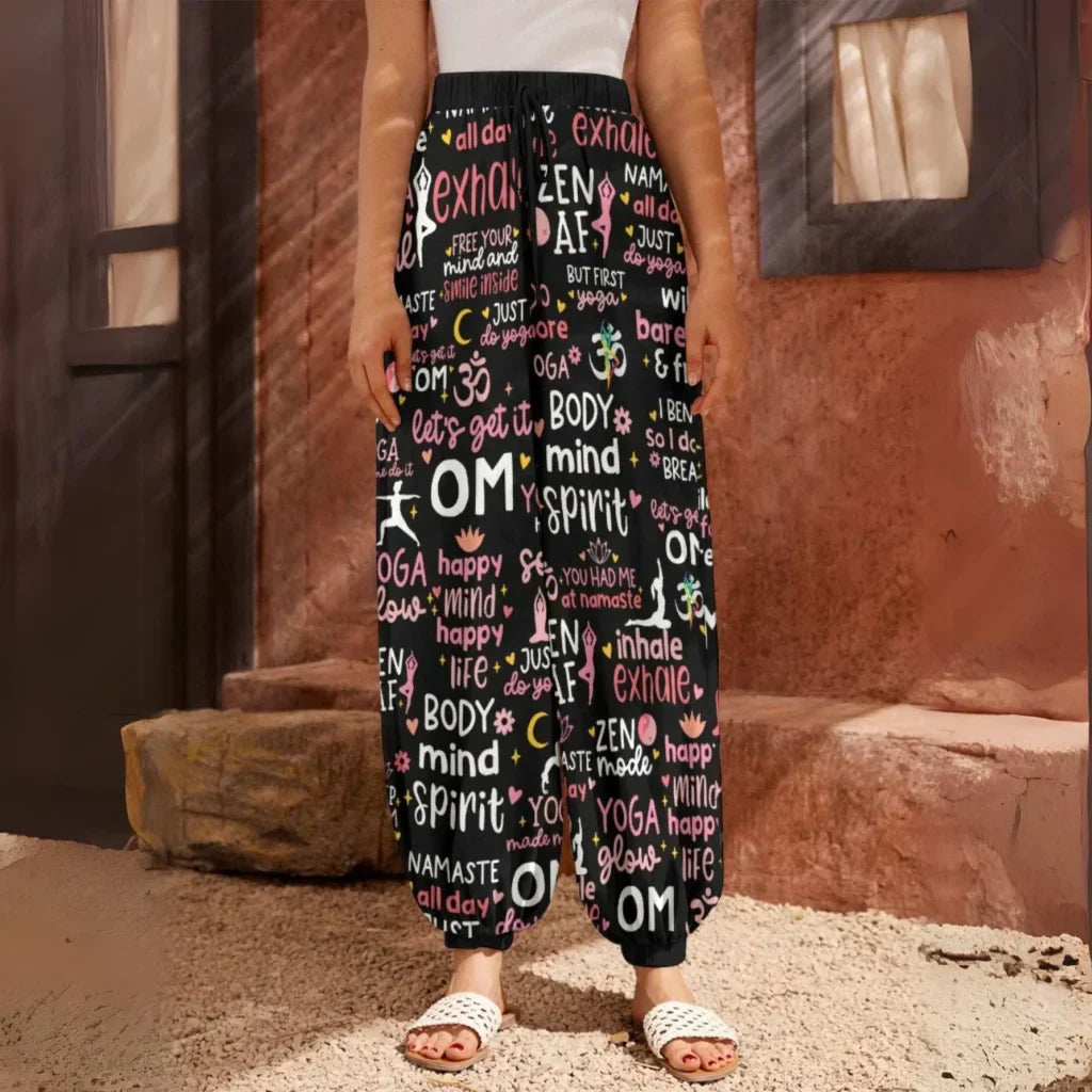 Loose-fitting harem pants with yoga-themed text and words printed all over in pink and white on black fabric, front view - YOGA QUOTES HAREM PANTS WOMEN - SPIRITUAL COMFORT